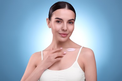 Photo of Beautiful woman with smear of body cream on her collarbone against light blue background