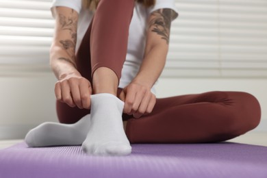 Photo of Woman putting on white socks on exercise mat indoors, closeup
