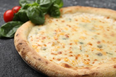 Photo of Delicious cheese pizza, basil and tomatoes on black textured table, closeup