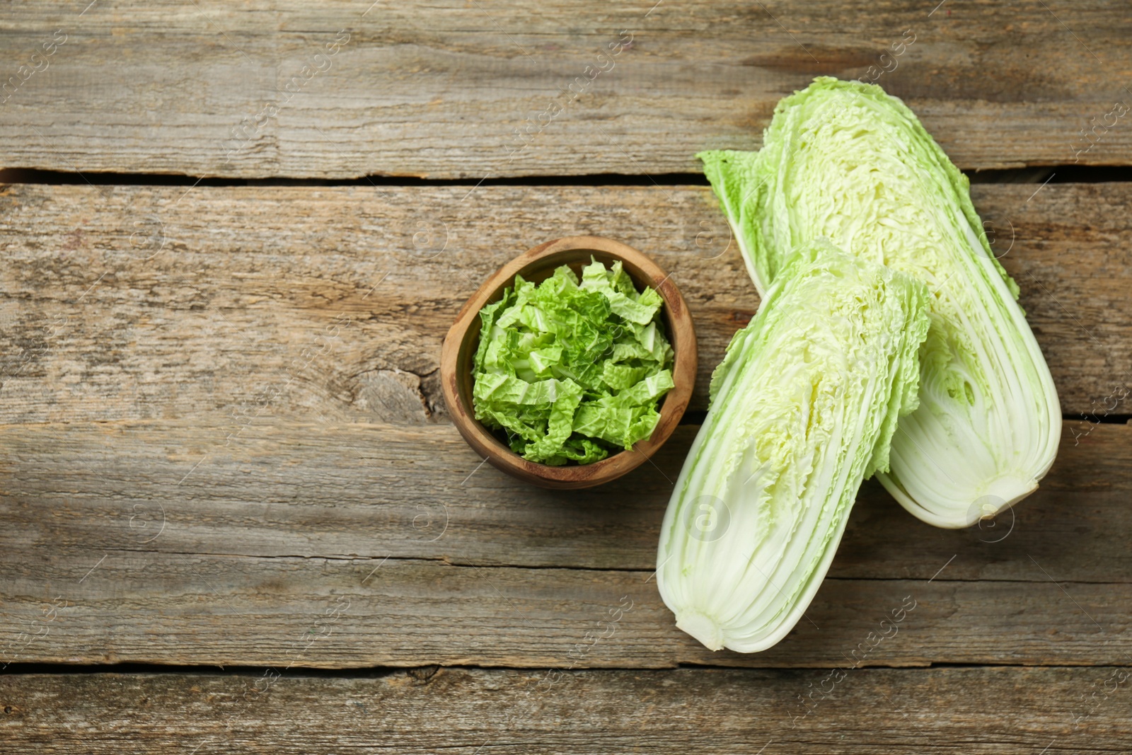 Photo of Whole and cut fresh Chinese cabbages on wooden table, top view. Space for text