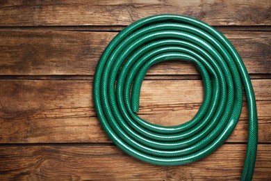 Photo of Green garden hose on wooden table, top view