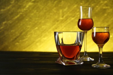 Photo of Different delicious liqueurs in glasses on dark wooden table, space for text