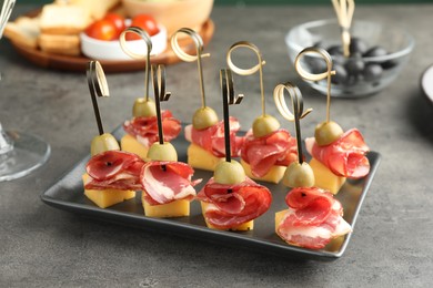 Photo of Tasty canapes with olives, prosciutto and cheese on grey table, closeup