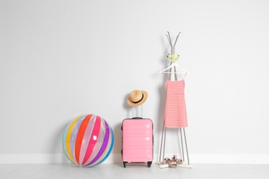 Photo of Suitcase with beach accessories near light wall. Space for text