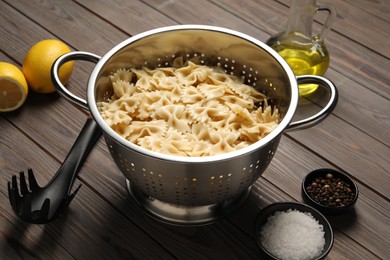 Cooked pasta in metal colander and spices on wooden table, closeup