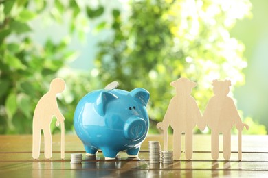 Pension savings. Figures of elderly people, piggy bank and stacked coins on wooden table outdoors