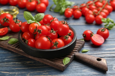 Photo of Fresh cherry tomatoes with basil in bowl on blue wooden table