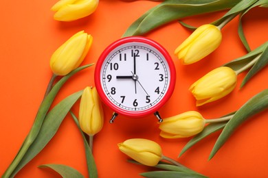 Photo of Red alarm clock and beautiful tulips on orange background, flat lay. Spring time