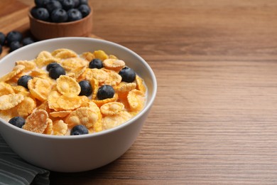 Photo of Bowl of tasty crispy corn flakes with milk and blueberries on wooden table, closeup. Space for text