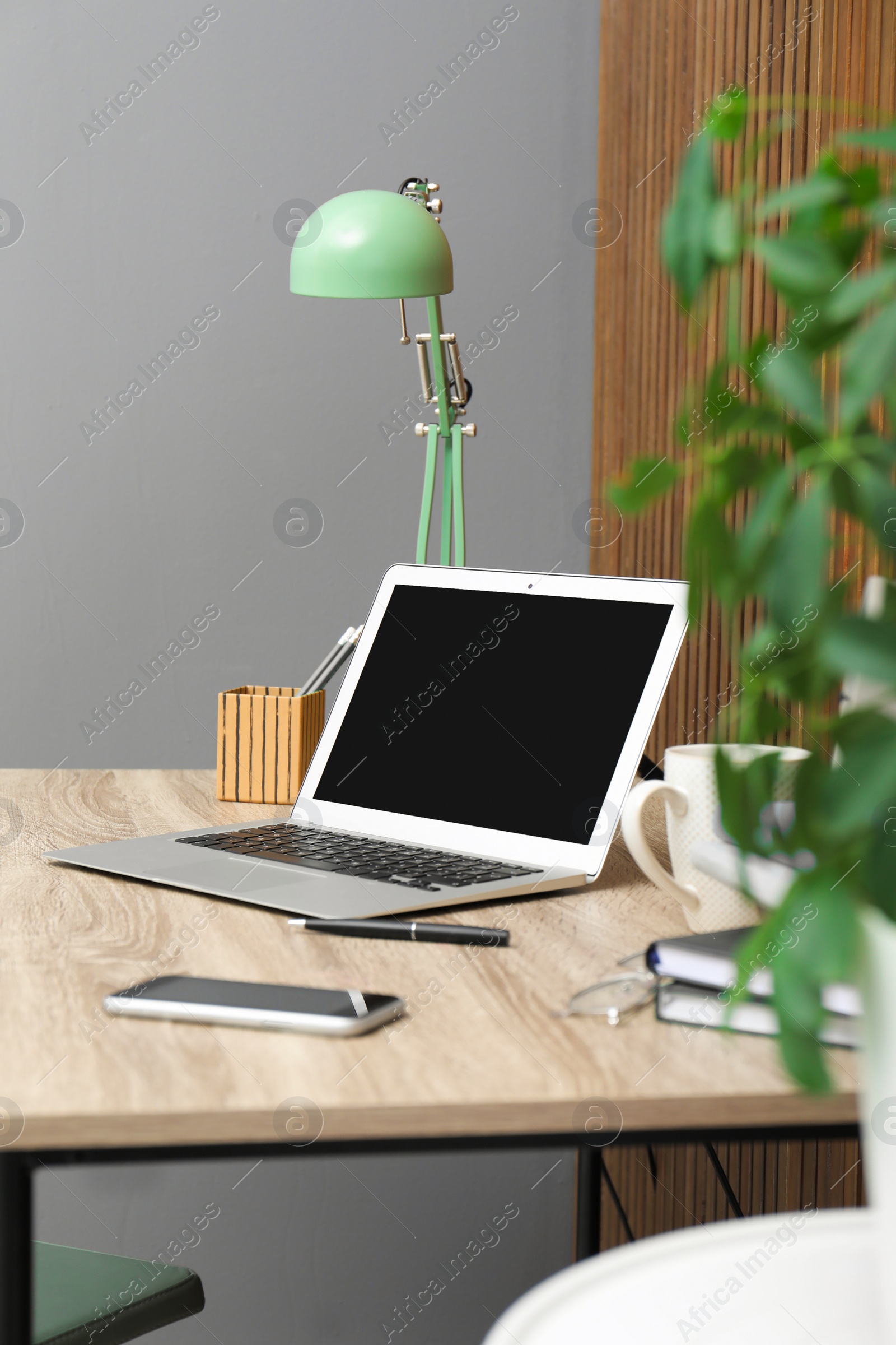 Photo of Stylish workplace interior with laptop on table near wooden wall. Space for text