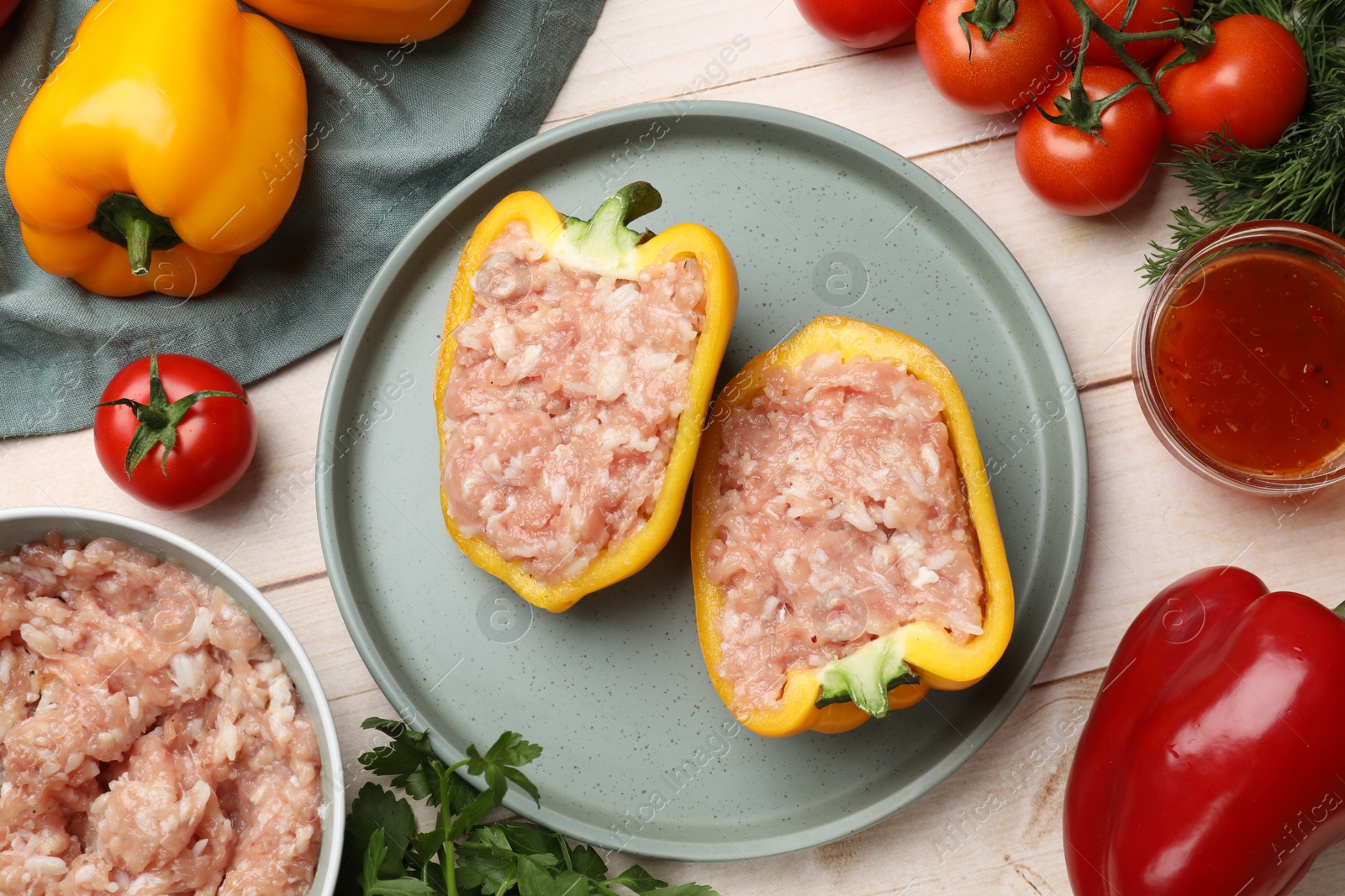 Photo of Raw stuffed peppers with ground meat and ingredients on light wooden table, flat lay