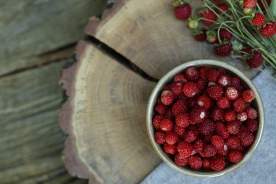 Photo of Bowl and tasty wild strawberries on wooden stump, top view. Space for text