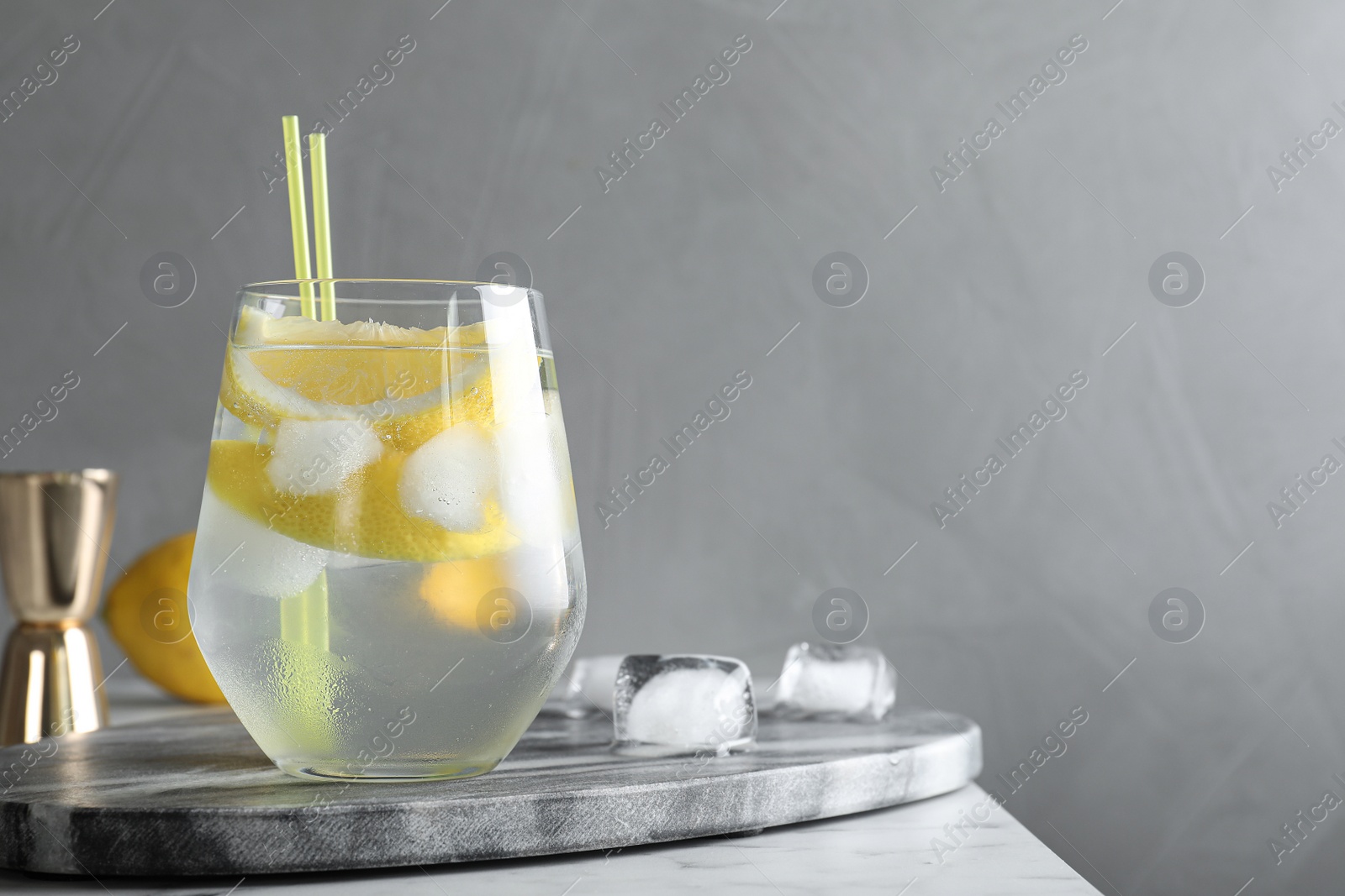 Photo of Glass of cocktail with vodka, ice and lemon on grey table. Space for text