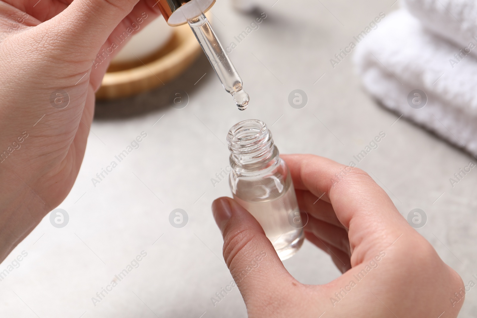 Photo of Woman with bottle of cosmetic serum and pipette at light table, closeup