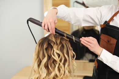 Photo of Hair styling. Hairdresser curling woman's hair in salon, closeup