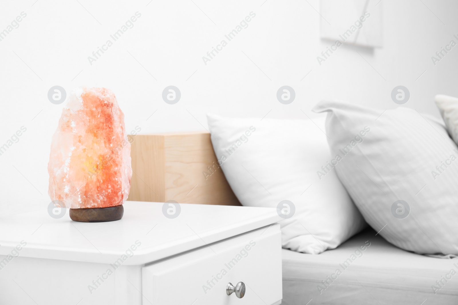 Photo of Himalayan salt lamp on white nightstand in bedroom. Space for text