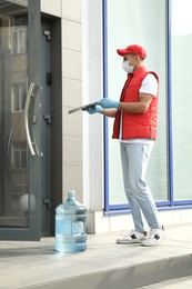 Photo of Courier in medical mask with clipboard and bottle for water cooler. Delivery during coronavirus quarantine