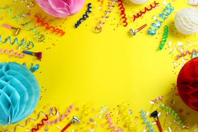 Photo of Frame of colorful serpentine streamers and other party accessories on yellow background, flat lay. Space for text