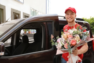 Delivery man with beautiful flower bouquet near car outdoors