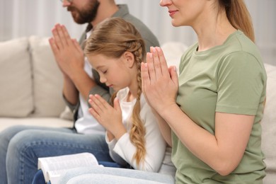 Photo of Girl and her godparents praying together on sofa at home