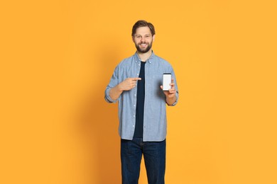 Photo of Man in casual clothes showing smartphone on orange background