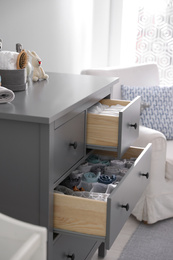 Photo of Modern open chest of drawers with clothes and accessories in baby room