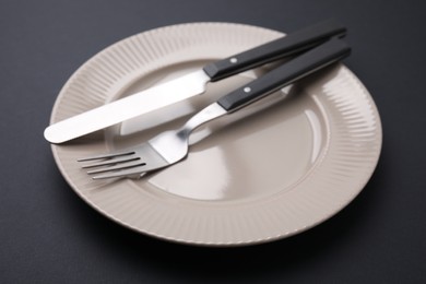 Clean plate with cutlery on black background, closeup