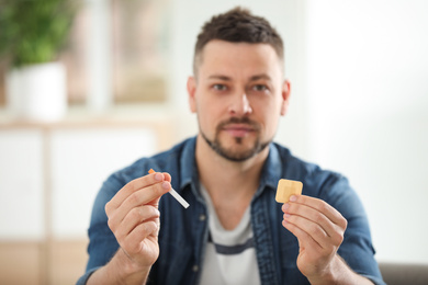 Photo of Man with nicotine patch and cigarette at home, focus on hands