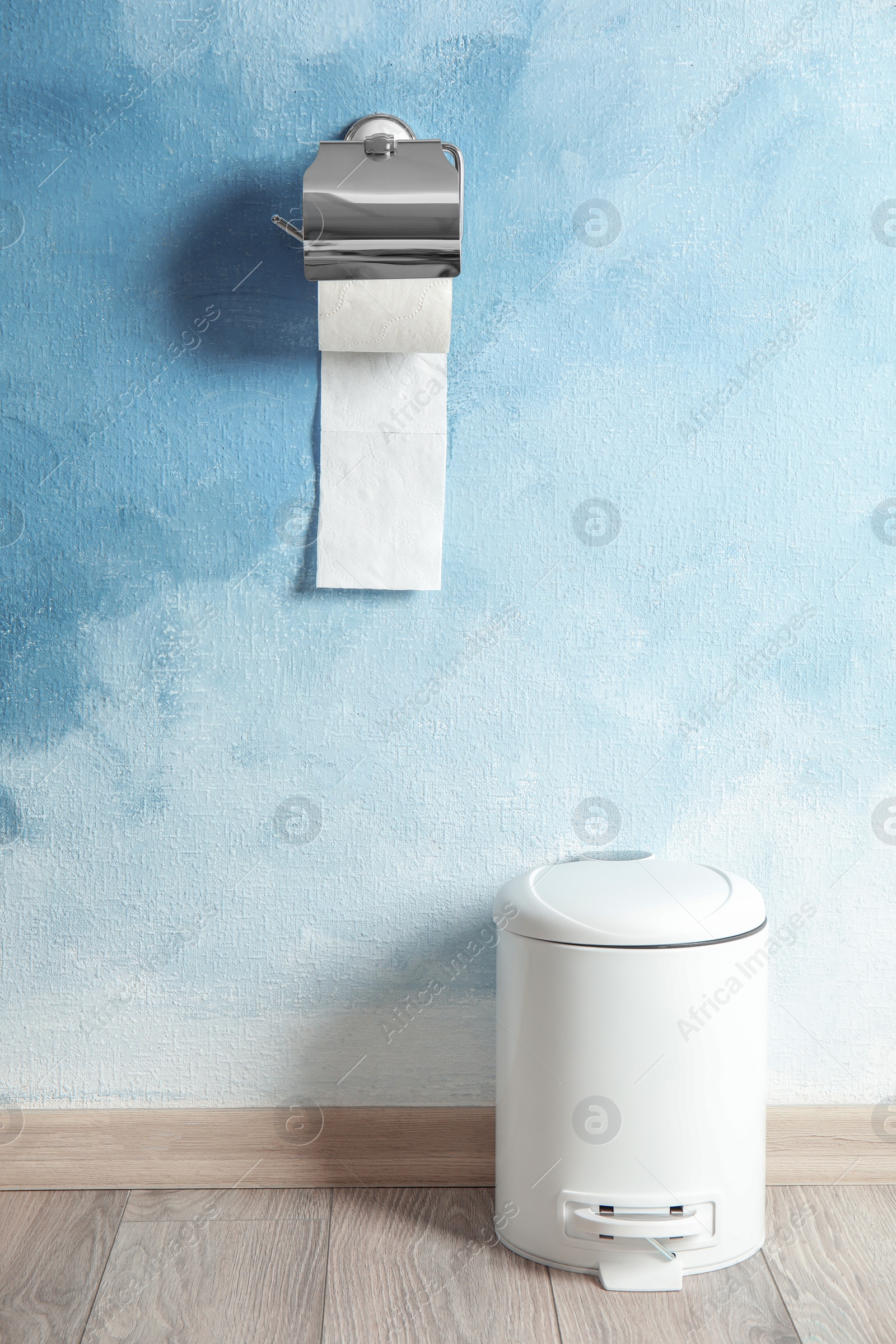 Photo of Toilet paper holder with roll and trash bin near color wall