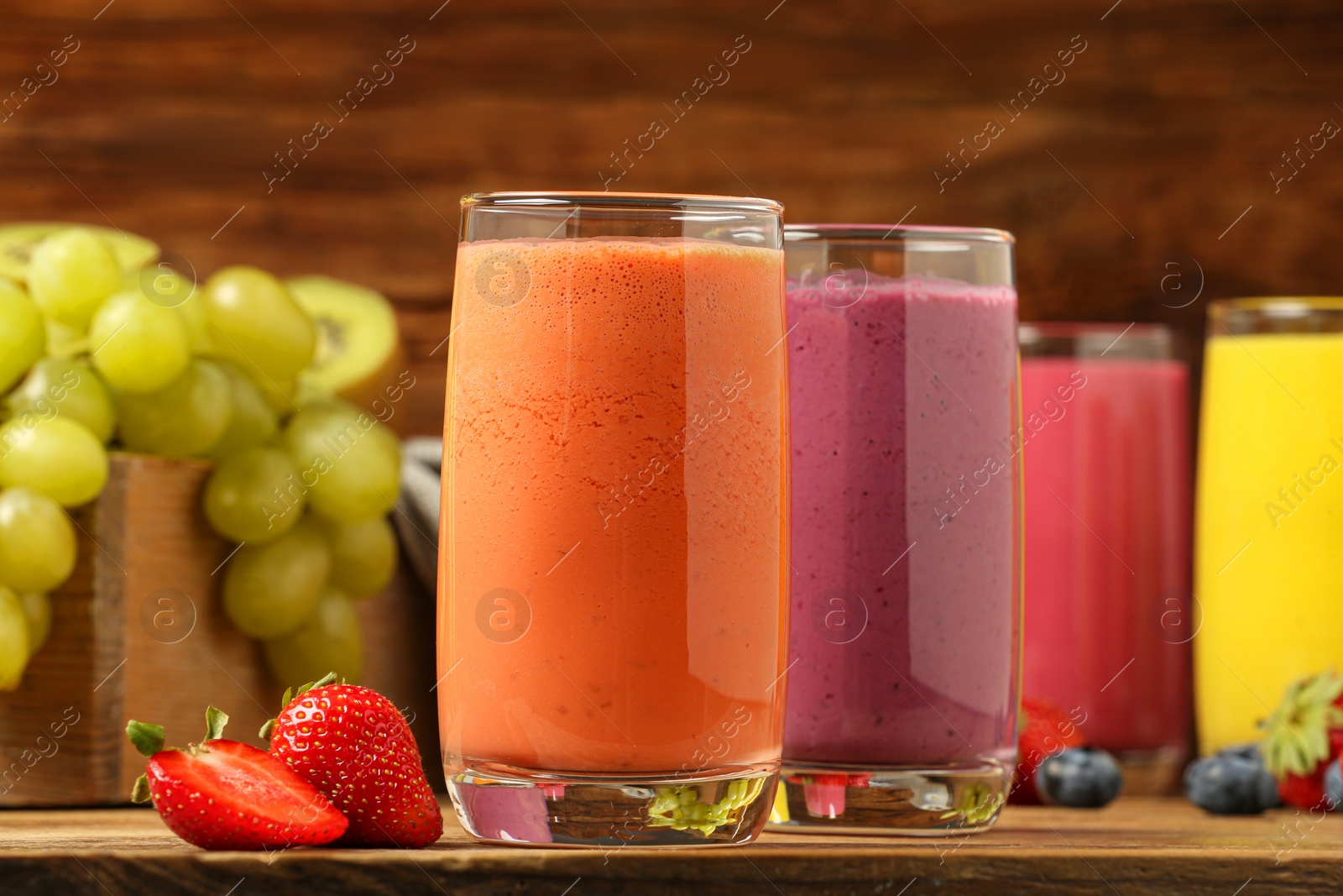 Photo of Glasses with different tasty smoothies and ingredients on wooden table