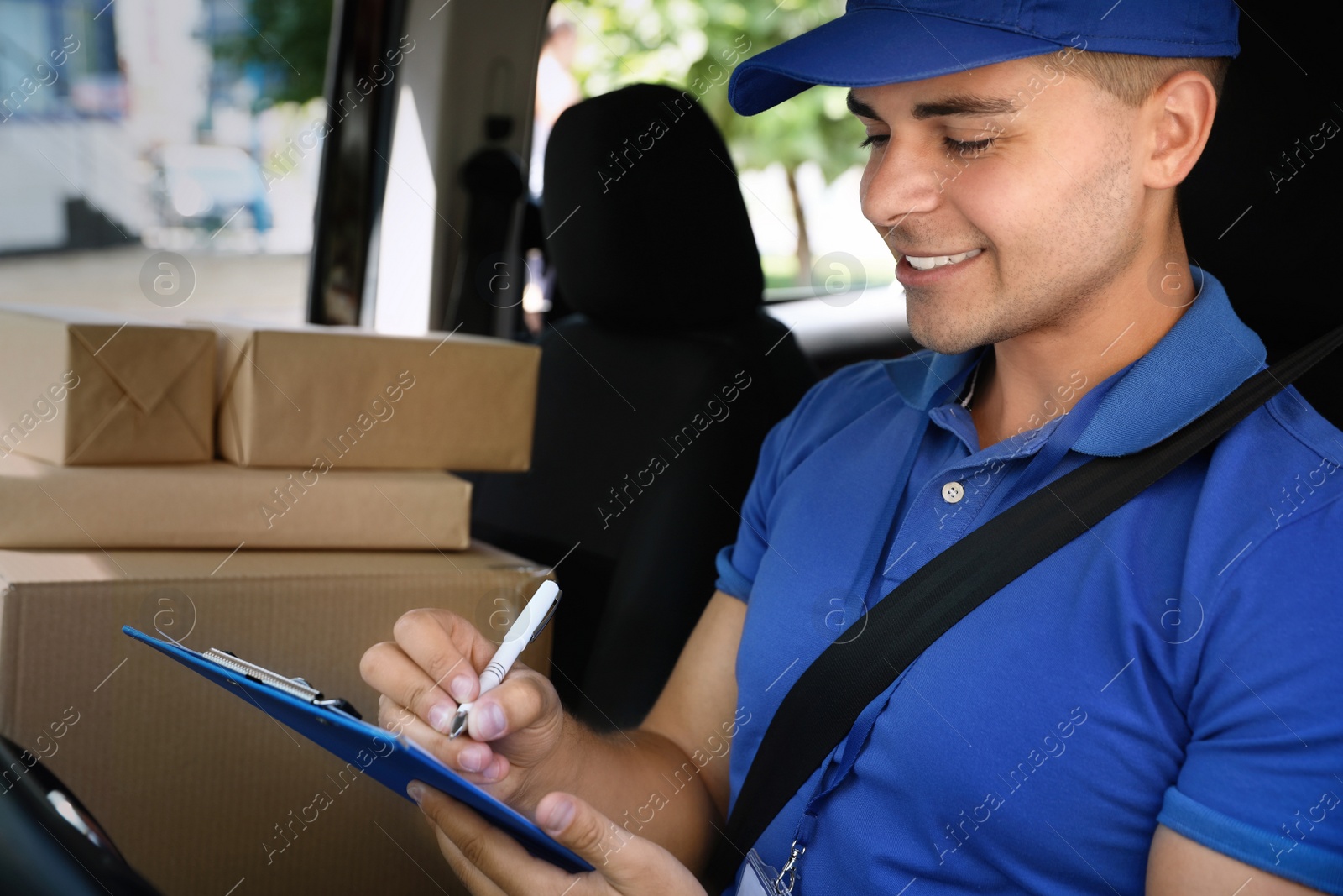 Photo of Young courier with parcels and clipboard in delivery car