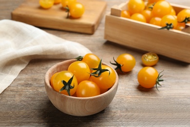 Photo of Ripe yellow tomatoes in bowl on wooden table