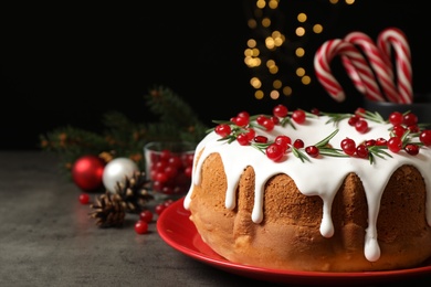 Traditional Christmas cake decorated with glaze, pomegranate seeds, cranberries and rosemary on grey table, space for text