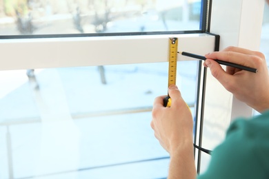 Photo of Service man measuring window for installation indoors, closeup. Space for text