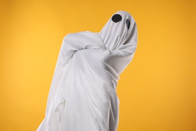 Photo of Creepy ghost. Person covered with white sheet on yellow background