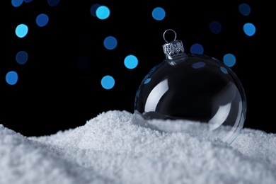 Photo of Transparent Christmas ball on snow against blurred fairy lights, space for text