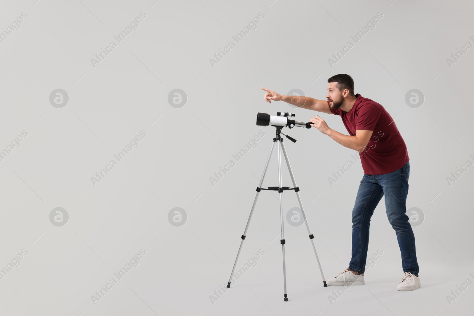 Photo of Excited astronomer with telescope pointing at something on light grey background. Space for text