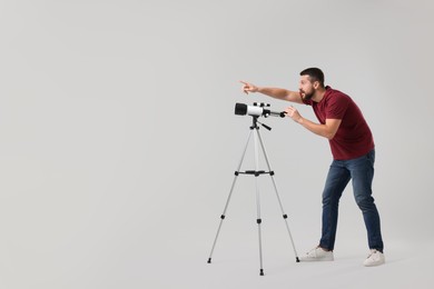 Excited astronomer with telescope pointing at something on light grey background. Space for text