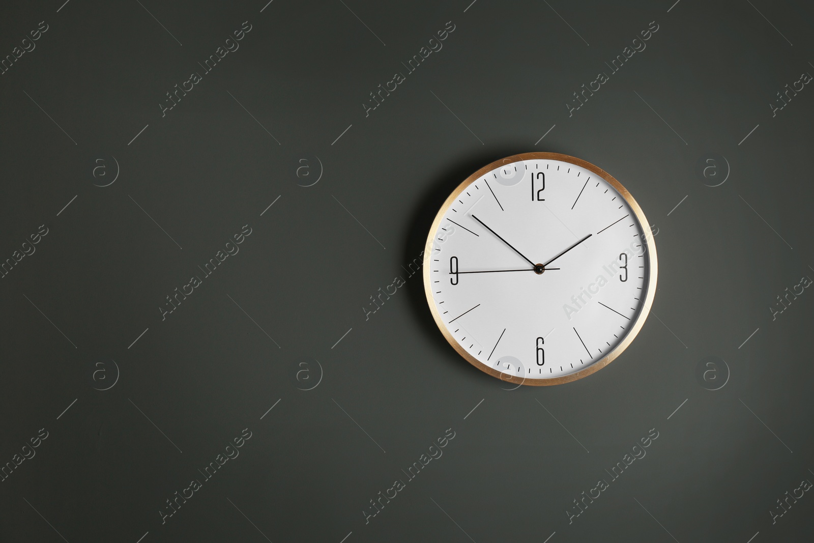 Photo of Stylish analog clock hanging on gray wall, space for text. Time of day