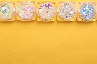 Photo of Jars with colorful shiny glitter on yellow background, flat lay. Space for text