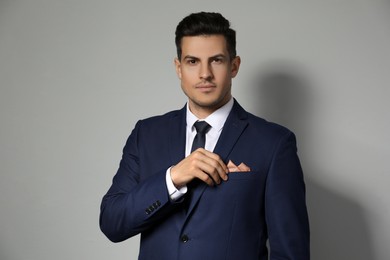 Man fixing handkerchief in breast pocket of his suit on light grey background