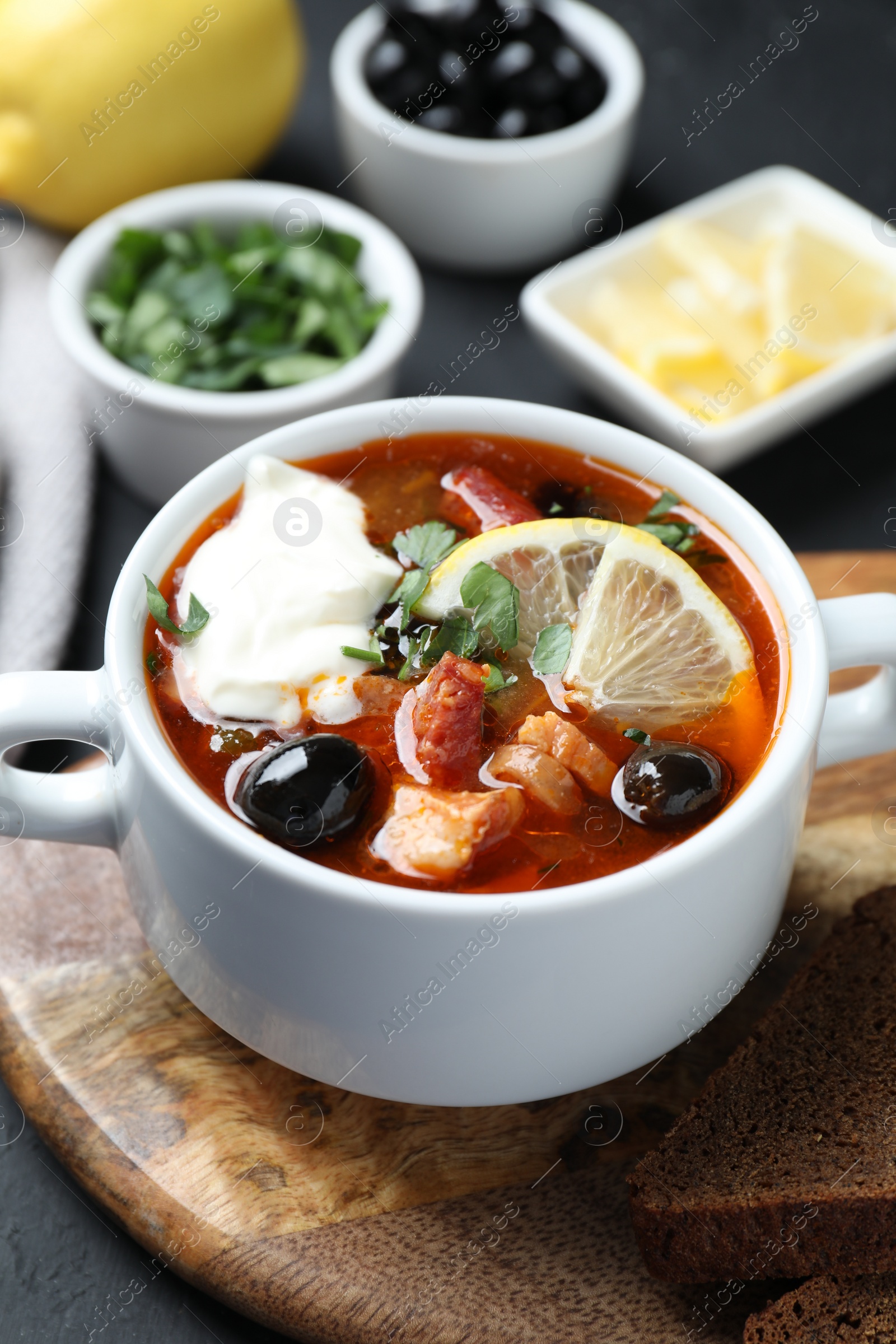 Photo of Meat solyanka soup with sausages, olives and vegetables in bowl served on dark grey table, closeup