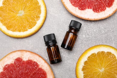 Photo of Bottles of essential oils with different citrus fruit slices on grey table, flat lay