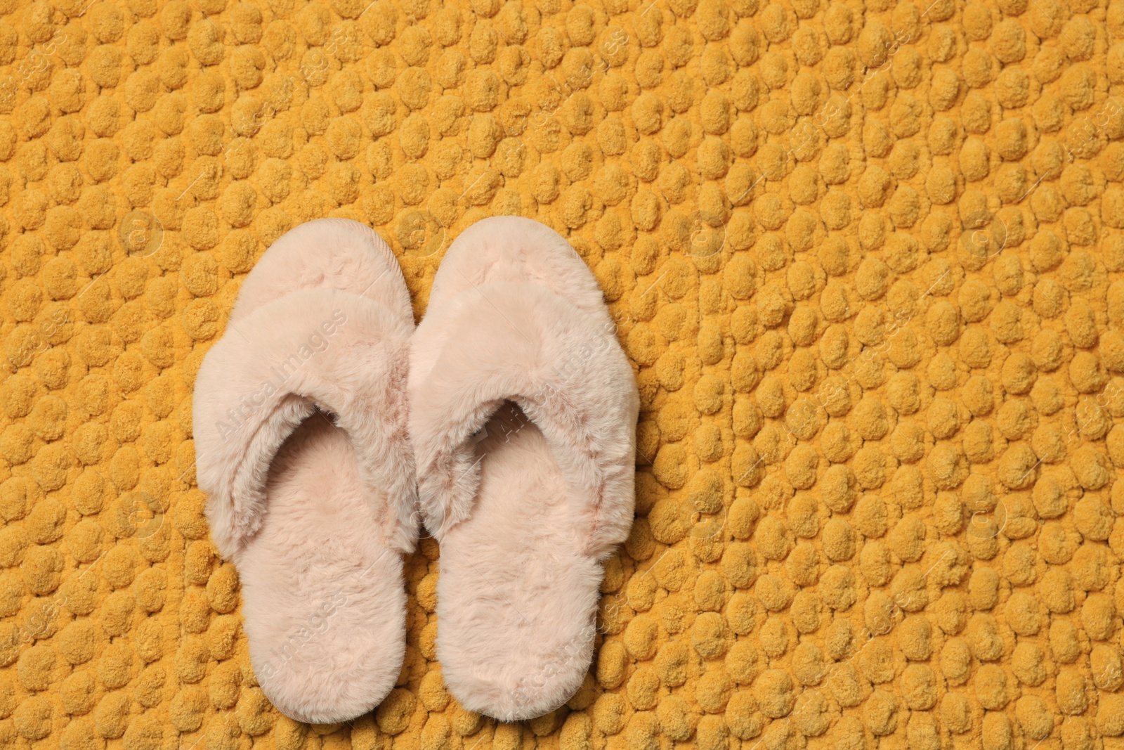 Photo of Slippers on soft orange bath mat, flat lay. Space for text