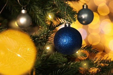 Photo of Beautiful shiny holiday baubles hanging on Christmas tree against blurred fairy lights, closeup