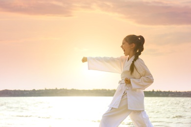 Cute little girl in kimono practicing karate near river