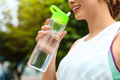 Young woman drinking water outdoors, closeup. Refreshing drink