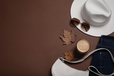 Flat lay composition with stylish hat and coffee on brown background, space for text