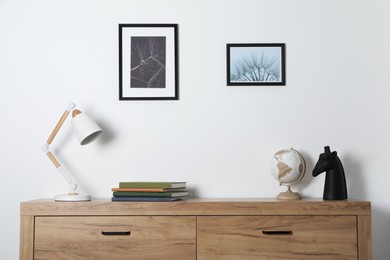 Photo of Desk lamp, books and decor on wooden chest of drawers indoors