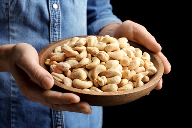 Photo of Woman holding bowl of cashew nuts on black background, closeup